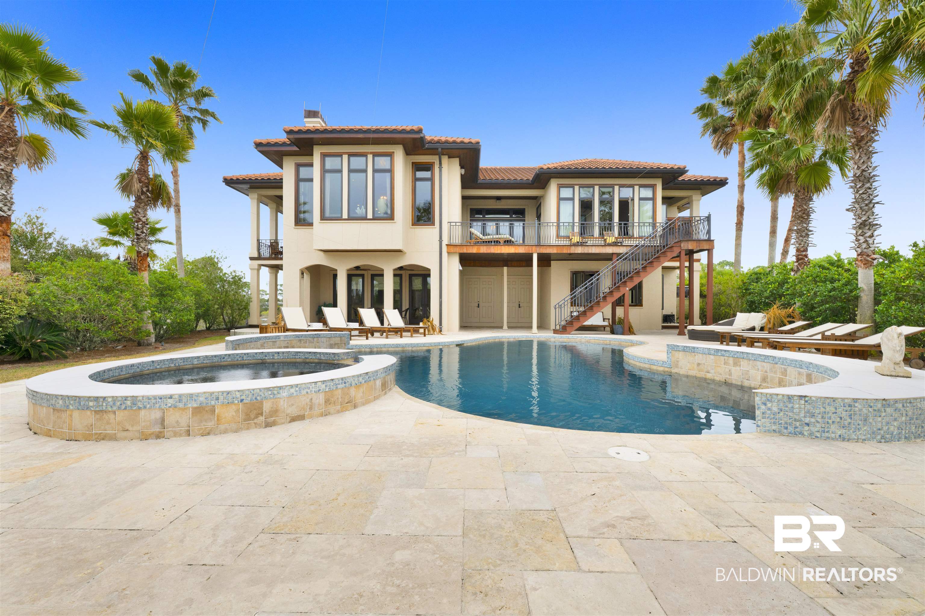Set on approximately 3.63 acres within the gated Ono Island community, this private waterfront residence offers substantial living space, quality construction, and protected deep-water access at the end of a cul-de-sac. The two-level home encompasses approximately 6,709 square feet with five bedrooms, five full baths, and one half bath, featuring a layout designed to support both full-time living and waterfront entertaining. Architectural elements include high pickled-pine ceilings, wide hallways, custom millwork, stone and wood flooring, and a private elevator providing access to both levels. The primary living spaces and chef’s kitchen are positioned on the upper level, while the lower level includes a theater room, den, and direct access to outdoor living areas. Connected to the main residence, the captain’s quarters include a sitting area, bedroom, and bathroom, offering flexible use as a private guest suite or secondary living space. Exterior amenities include a heated gunite pool, summer kitchen, covered and open patios, outdoor shower, and landscaped grounds. Boating features include a covered 15’ x 111’ boathouse with lift and power, offering safe harbor at the mouth of the canal with bay access. Additional highlights include a generator, zoned HVAC, and attached garage. Situated within Ono Island with private security and community amenities, this property presents a rare combination of acreage, waterfrontage, and boating infrastructure. There is a $8,000.00 Admission Fee to Ono Island. Buyer to verify all information during due diligence.