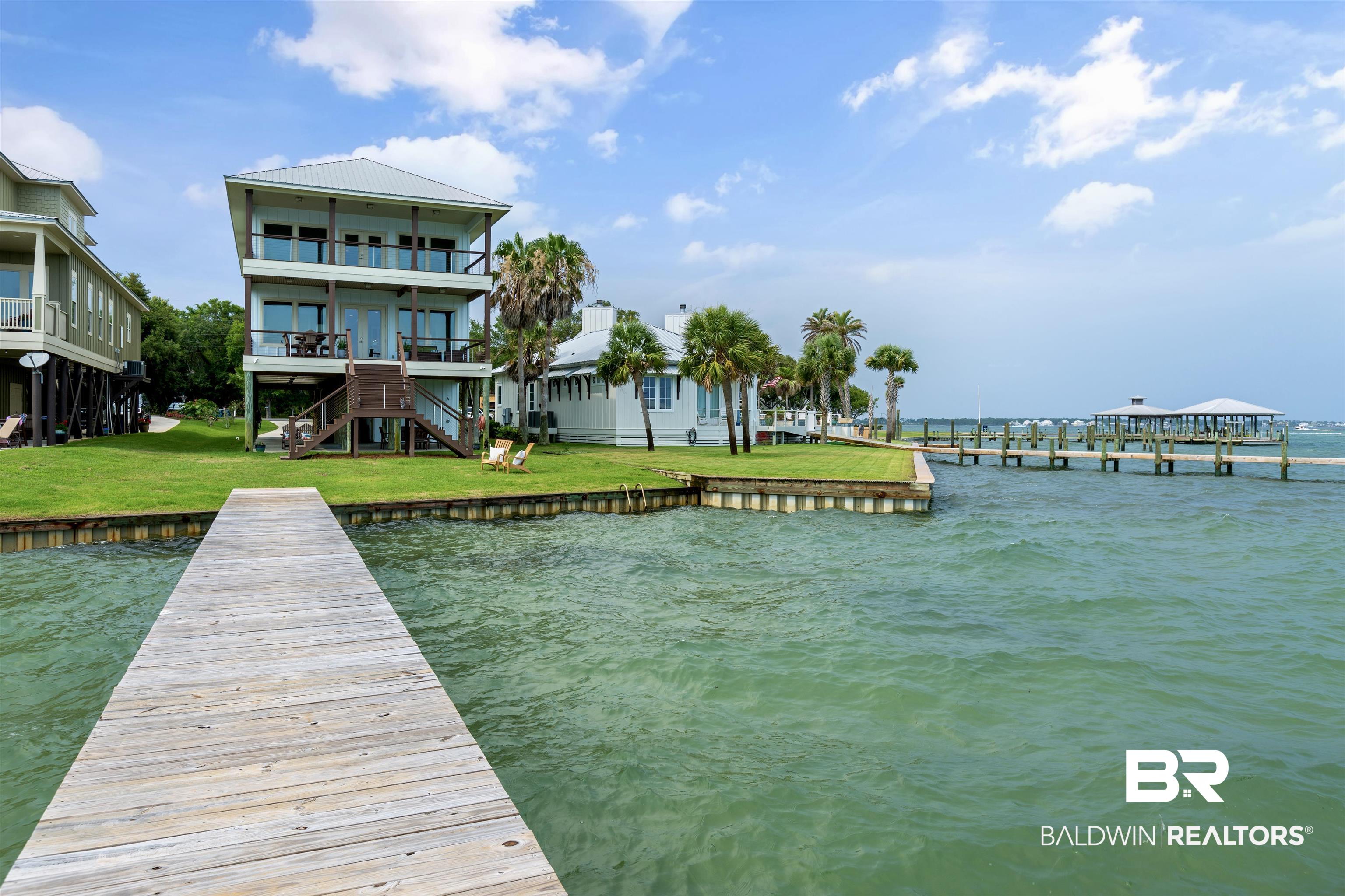 Remarkable waterfront residence boasting unparalleled panoramic bay views of Bayou St. John. Located within Bear Point Estates, this residence invites you to indulge in a desirable waterfront lifestyle observing the Blue Angels, seeking aquatic adventures, going for a leisurely swim, setting sail from your private pier, or taking a golf cart for an evening of waterfront dining. The interior is thoughtfully designed with an expansive open-concept layout with breathtaking bay views. The kitchen, appointed with a gas range, custom cabinets by Julian Brock, stainless steel appliances, and exquisite granite countertops, serves as the heart of the home. A center island provides both functionality and aesthetic appeal, while curved front Apron sink adds a touch of style. Each bedroom features an ensuite bathroom and generous walk-in closets. The primary suite offers a spa-inspired bathroom complete with a soaking tub and walk-in shower. Design highlights include two antique doors by Charles Phillips, a custom-made handrail, cable railings for unobstructed bay views, Birch floors and 8” trim and molding. Additional highlights include a bay front bonus room with a private balcony, two second level storage rooms, outdoor shower and ground-level half bath. For the avid boater or those seeking easy access to the Gulf of Mexico, this location is ideal. Buyer to verify all information during due diligence.