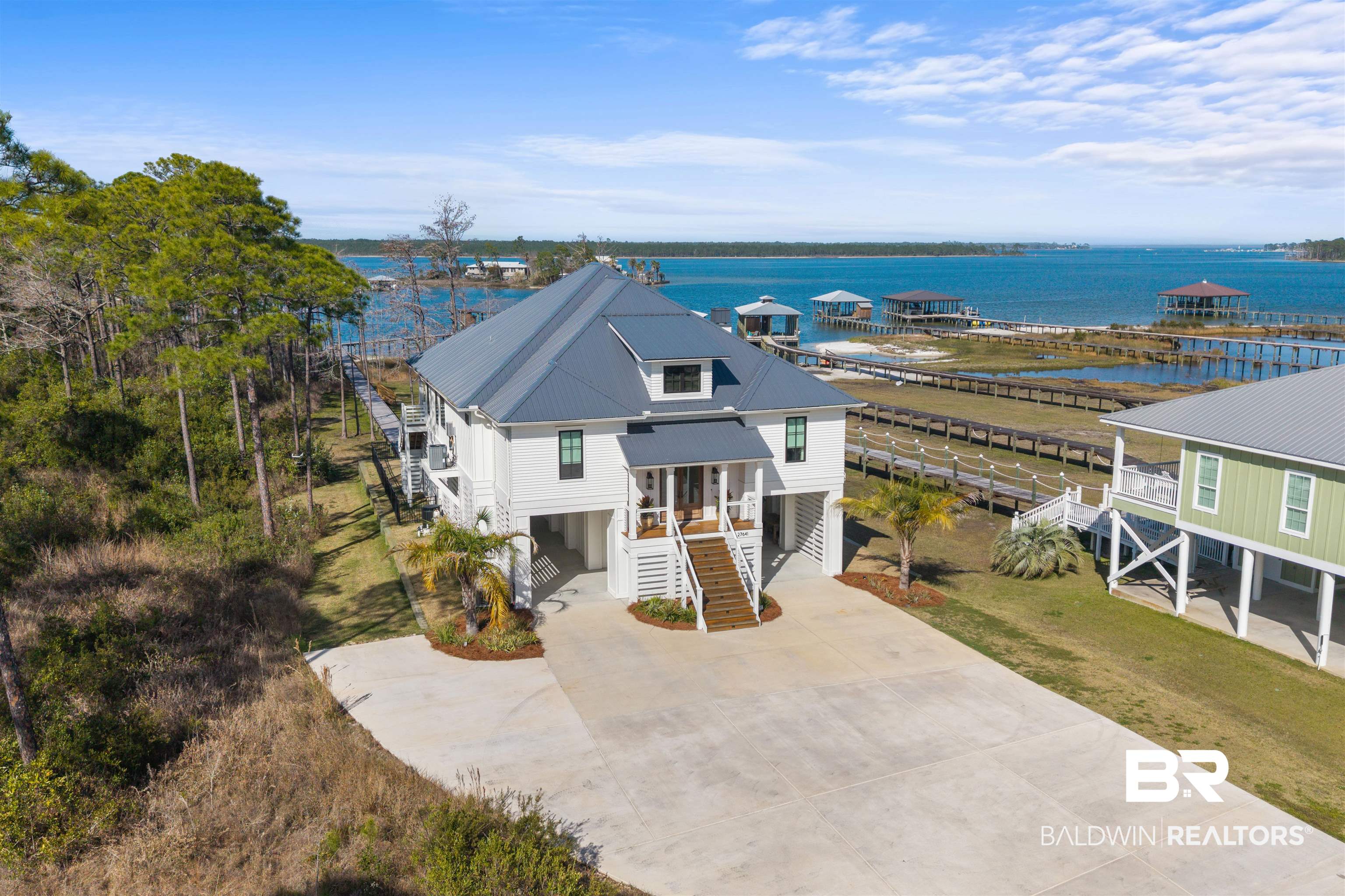 Welcome to your private waterfront retreat overlooking beautiful Bay La Launch in the protected waters of Cypress Cove. Situated on an expansive 1.86-acre lot, located in an X Zone, this stunning raised coastal home offers approximately 3,400 square feet of thoughtfully designed living space with breathtaking bay views from nearly every angle. This exceptional property features 5 spacious bedrooms and 4.5 bathrooms, providing ample room for family and guests. Inside, you’ll find engineered hardwood flooring throughout, complemented by custom window treatments and a warm, inviting wood/gas-burning fireplace that anchors the main living area. The gourmet kitchen is equipped with stainless steel appliances, perfect for entertaining or everyday coastal living. Modern conveniences include an on-demand hot water system, two HVAC units, and a 24kW whole-house generator for peace of mind year-round. Step outside and experience resort-style waterfront living. The property boasts a 20x30 saltwater gunite pool complete with a heating and cooling system, creating the perfect environment for relaxing or entertaining in every season. The fully irrigated yard and generous acreage provide privacy and space rarely found on the water. Boating enthusiasts will appreciate the impressive 40x30 covered boathouse featuring a swim platform, 12,000 lb GEM remote boat lift, and jet ski lift, making it effortless to enjoy the surrounding waters. Additional features include an enclosed tool room and abundant storage for all your coastal gear. Built to the Gold Fortified standard, this home offers enhanced durability and potential insurance savings while delivering luxury coastal living at its finest. With panoramic views across Bay La Launch, protected waters for boating, and exceptional amenities throughout, this property is truly a rare waterfront opportunity. Buyer to verify all information during due diligence.