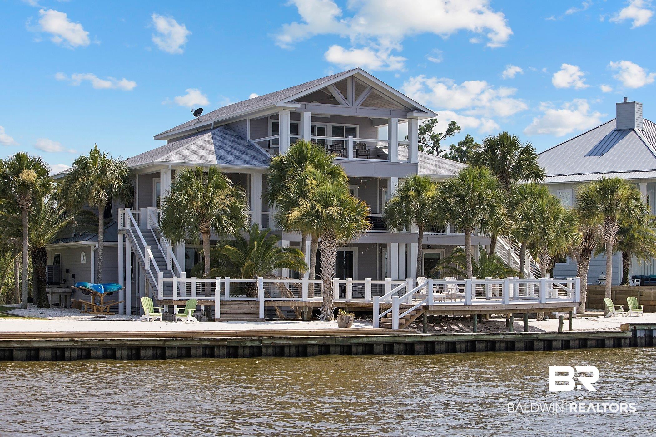 This magnificent custom-built East Orange Beach home is the perfect boater’s and entertainer’s delight. With 211 ft of water frontage directly on Bay La Launch, it overlooks the natural beauty of wooded land across the bay. With over 5000 sqft, this 4 bed and 4 ½ bath home features high end amenities, including your own private beach and pier.   Through the custom Brazilian Oak front door, the spacious split foyer greets you with oak hardwood floors and a vaulted ceiling.  On the main level, you will enjoy the oversized great room, kitchen, and 7-seat home theater. Expansive sliding glass doors that open onto large balconies are present in the living areas and every bedroom, allowing you to enjoy the view of the bay from anywhere in the home. The primary suite is a luxury retreat with oak wood flooring and a tray ceiling, featuring a large walk-in custom closet and a bright, inviting bathroom with quartz countertops, a freestanding single slipper tub, and a walk-in rain shower.   On the 1st floor, there is a second large great room with sliding glass doors that open onto another expansive balcony and deck looking out over the bay. There is a mini kitchen, laundry room, and two additional large bedrooms, each with a private en suite.  On the 3rd floor, you will enjoy an oversized bedroom with a vaulted wood ceiling, private balcony, and bathroom.   This home also boasts an elevator, a new pier and boat house built with a new 10,000 lb. lift, a separate lift for 2 jet skis, 4 car garage, 2 on-demand natural gas water heaters, 2 HVAC units replaced in 2020 & 2021, new kitchen appliances, new roof installed in 2021, new exterior paint in 2021, keyless entry doors, Bahama shutters, impact rated sliding glass doors, hurricane shutter on entry door, expansive wood deck and walkways all with see-through cable railing, a private sandy beach, security and 6-camera DVR system, sprinkler system with iron filtration, and palm trees throughout the well-manicured grounds.  No HOA