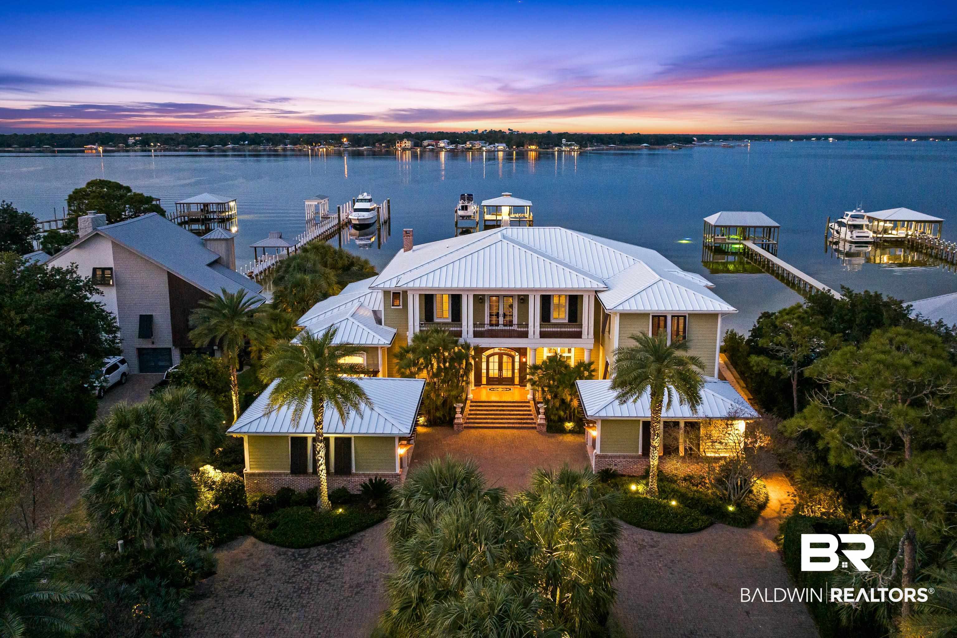 Welcome to 30147 Ono Blvd in Orange Beach, AL. This stunning home is perfectly nestled along the shores of Bayou St John on one of the most desirable streets on Ono Island. Featuring five bedrooms with five full bathrooms, three half bathrooms, and 7,840 square feet, this luxurious custom built home offers a beautiful blend of traditional elegance and serene waterfront living, which creates the perfect private oasis with a touch of Southern charm! The heart of this home is the spacious open-concept living area that seamlessly connects the indoor space with its coastal outdoor environment. The main level features beautifully detailed 12' ceilings, a large living room and dining room, the primary suite, an office, a handcrafted pub for gathering, and a chef's kitchen with a keeping room, gas fireplace, butler’s pantry, and utility room. The kitchen features pecky cypress ceilings, two large islands with granite countertops, under cabinet and toe kick lighting, Rohl faucets, and custom cabinetry. The primary suite offers stunning views of Bayou St. John with direct access to the patio and a massive spa-like bathroom with his and her walk-in closets. The second level features four guest suites, a bunk room, additional laundry room, and a separate living room with a kitchen and access to a spacious balcony offering breathtaking views. No expenses nor details were spared in this home featuring top shelf finishes and appliances, elegant crown molding throughout, luxurious tile plank floors, cabinetry by Julian Brock, hand-crafted Rohl faucets, eight foot solid mahogany wood interior doors, an elevator, geo-thermal heating and air conditioning system, and a 50kW whole home generator. The exterior features an amazing outdoor living space with a fully equipped kitchen, fireplace, heated saltwater pool and spa, a private beach area, aluminum heavy gauge standing seam roof, 40x40 covered boat house with ThruFlow decking, a storage room and two boat lifts. Buyer to verify all in